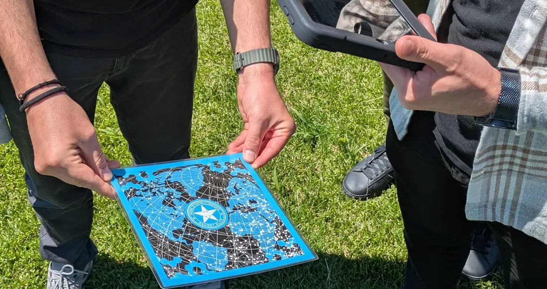 A team compares a printed star map with clues on a tablet during a Salty Soil outdoor AR escape game in Thessaloniki