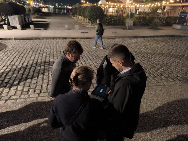 A team checks the tablet at night on the Thessaloniki waterfront during a Salty Soil AR escape game