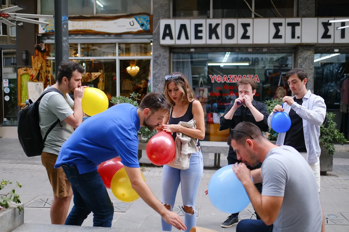 Team members race to blow up balloons on a Thessaloniki shopping street during a Salty Soil city treasure hunt challenge