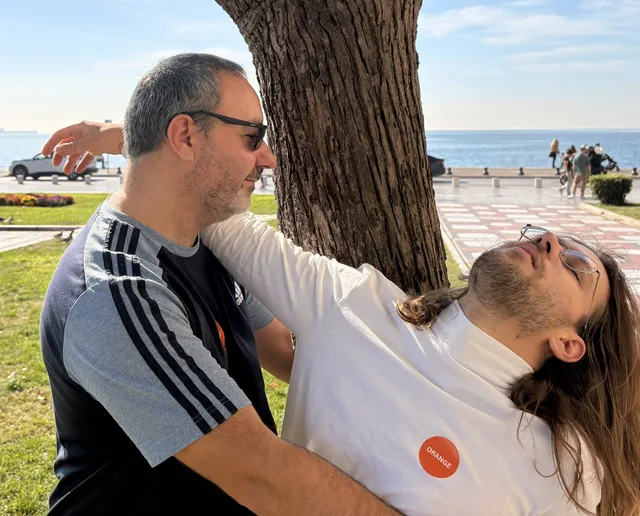 Two colleagues act out a pose against a tree on the Thessaloniki waterfront for a photo challenge during a Salty Soil city treasure hunt