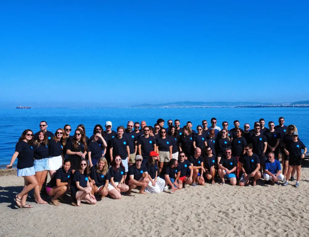 A large corporate group in matching T-shirts on a beach on the Thermaic Gulf, with Thessaloniki across the water, during a company retreat run by Salty Soil