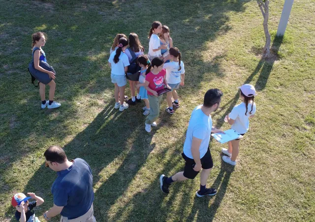 Αεροφωτογραφία παιδιών και γονέων που παίζουν Magic Portal με tablet και φύλλα στοιχείων σε ένα πάρκο, ένα οικογενειακό AR escape game της Salty Soil.
