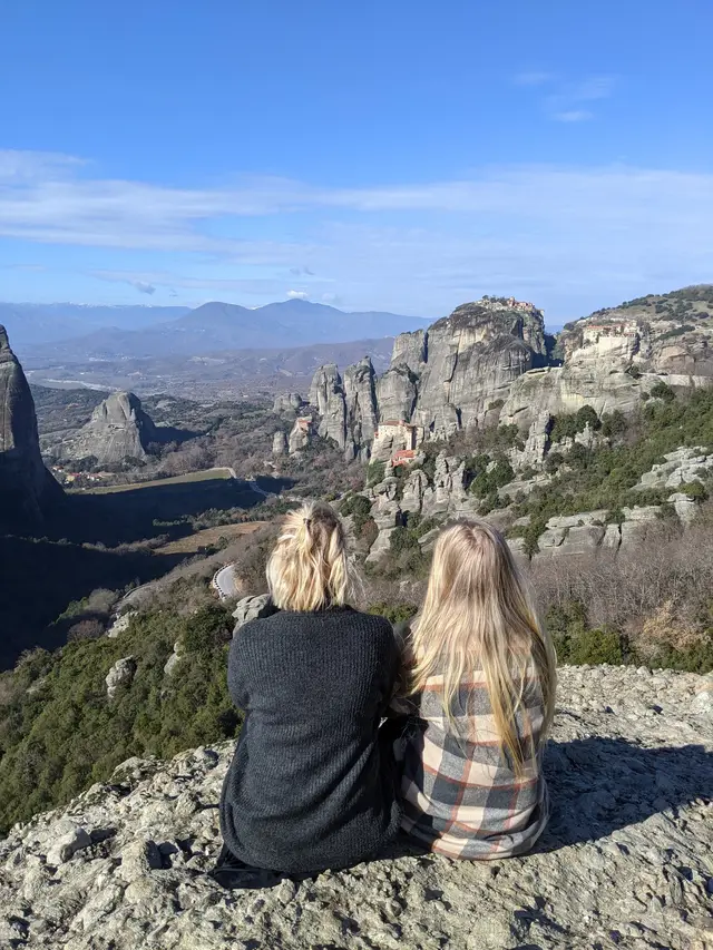 Two guests sit at a viewpoint looking over the Meteora monasteries and the valley on a Salty Soil day trip from Thessaloniki