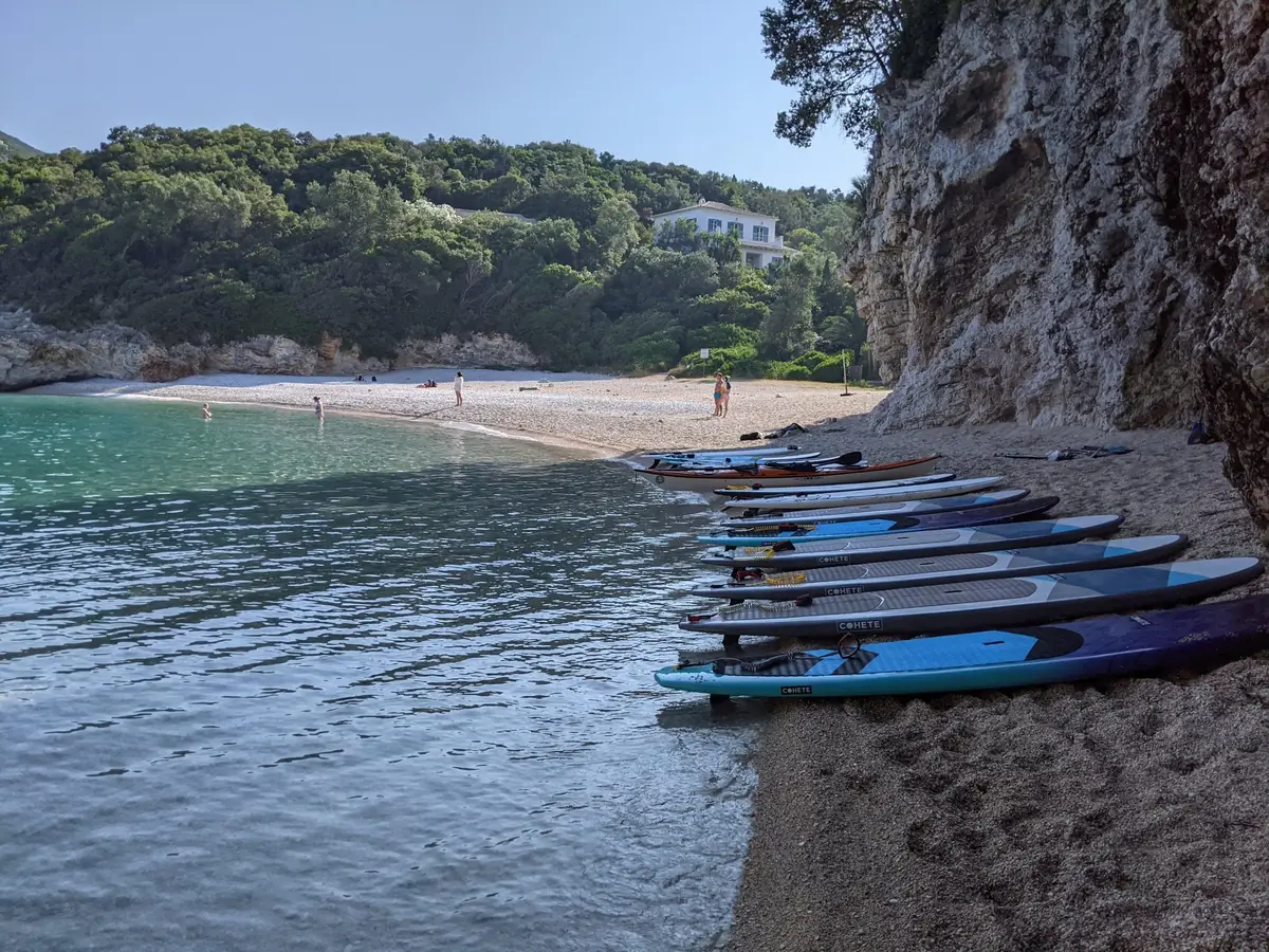 A row of SUP boards rests on a quiet beach below a cliff, during a picnic stop on a Salty Soil multi-day SUP trip