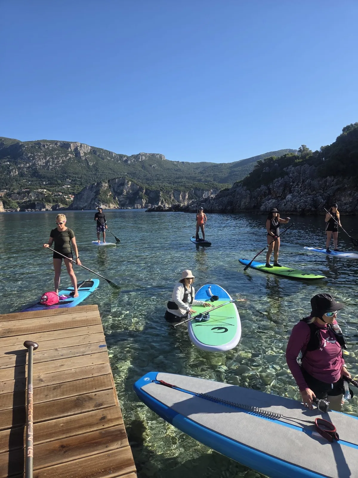 Κωπηλάτες ξεκινούν με σανίδες SUP από μια μικρή προβλήτα πάνω από κρυστάλλινα νερά στην Παλαιοκαστρίτσα της Κέρκυρας, σε πολυήμερη εκδρομή SUP της Salty Soil
