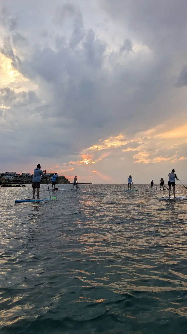 Paddlers stand on their SUP boards under a dramatic sunset sky on a Salty Soil multi-day SUP trip in Greece