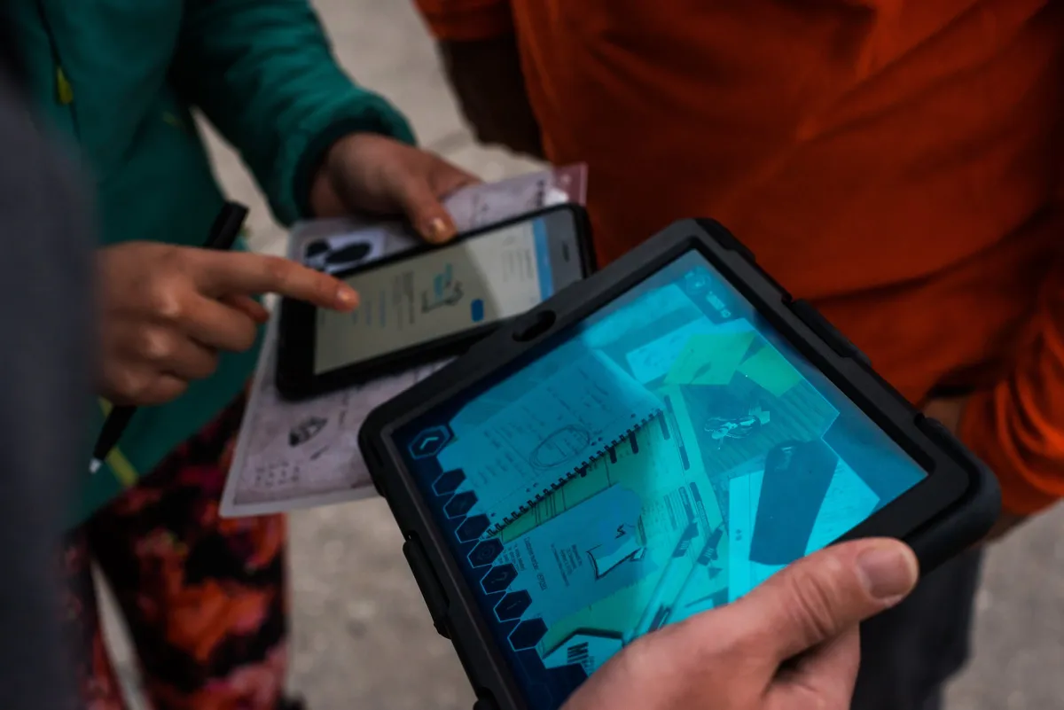 Κοντινό πλάνο του tablet του Operation Mindfall με απόρρητους φακέλους σε επαυξημένη πραγματικότητα, δίπλα σε ένα κινητό και έντυπα στοιχεία, σε ένα AR escape game της Salty Soil.