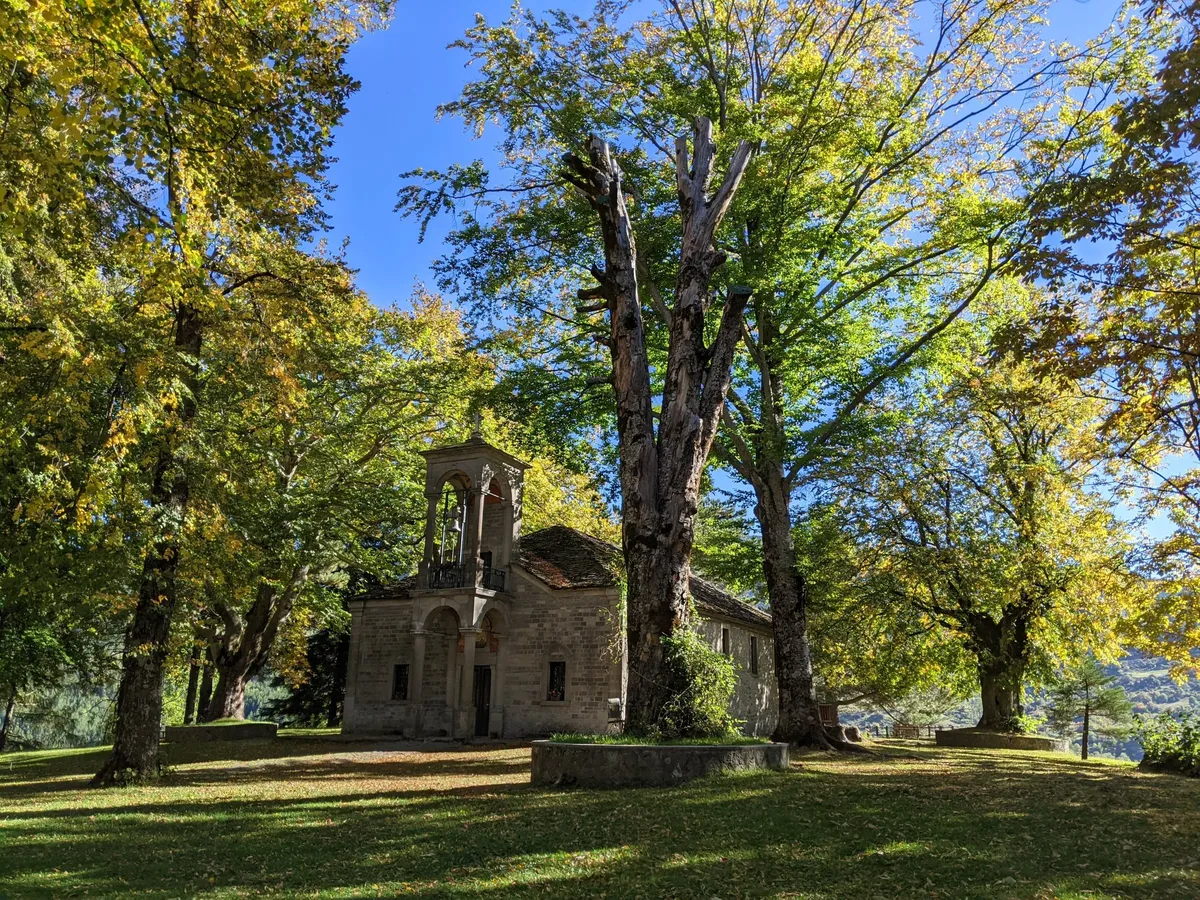 The stone chapel of Agios Georgios among tall autumn trees in Metsovo, Epirus, on a Salty Soil private multi-day tour of Greece