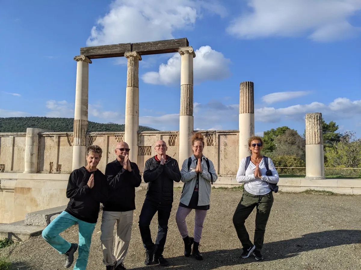 A group of guests strikes a yoga pose in front of the restored colonnade at the Sanctuary of Asklepios in Epidaurus, on a Salty Soil private tour