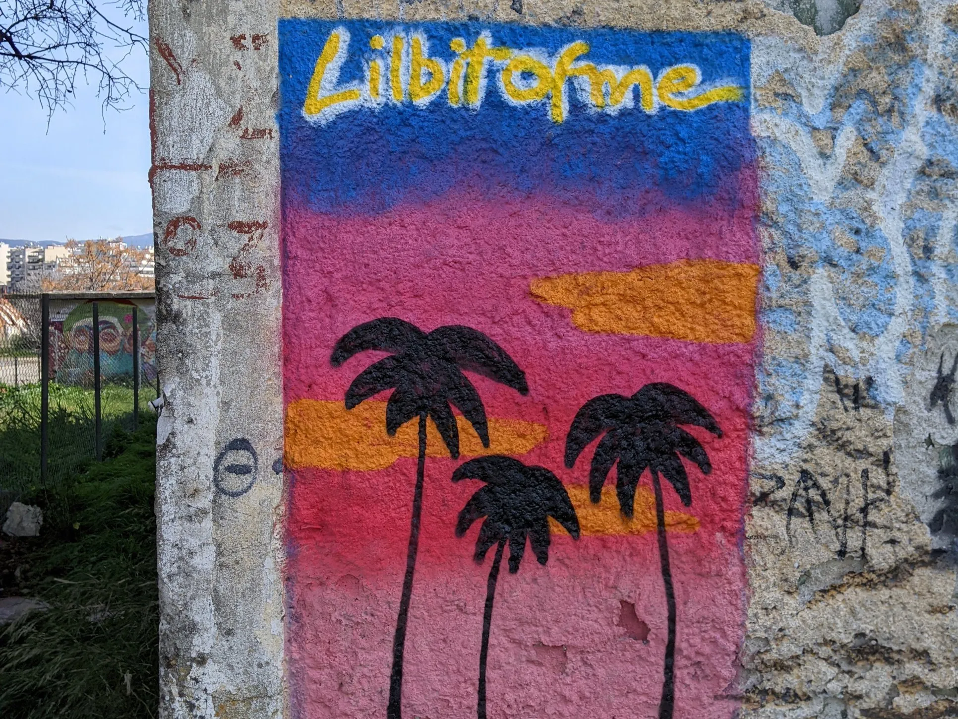 Μικρό έργο street art με μαύρους φοίνικες σε ροζ και μπλε ουρανό, ζωγραφισμένο σε έναν παλιό πέτρινο τοίχο στη Θεσσαλονίκη