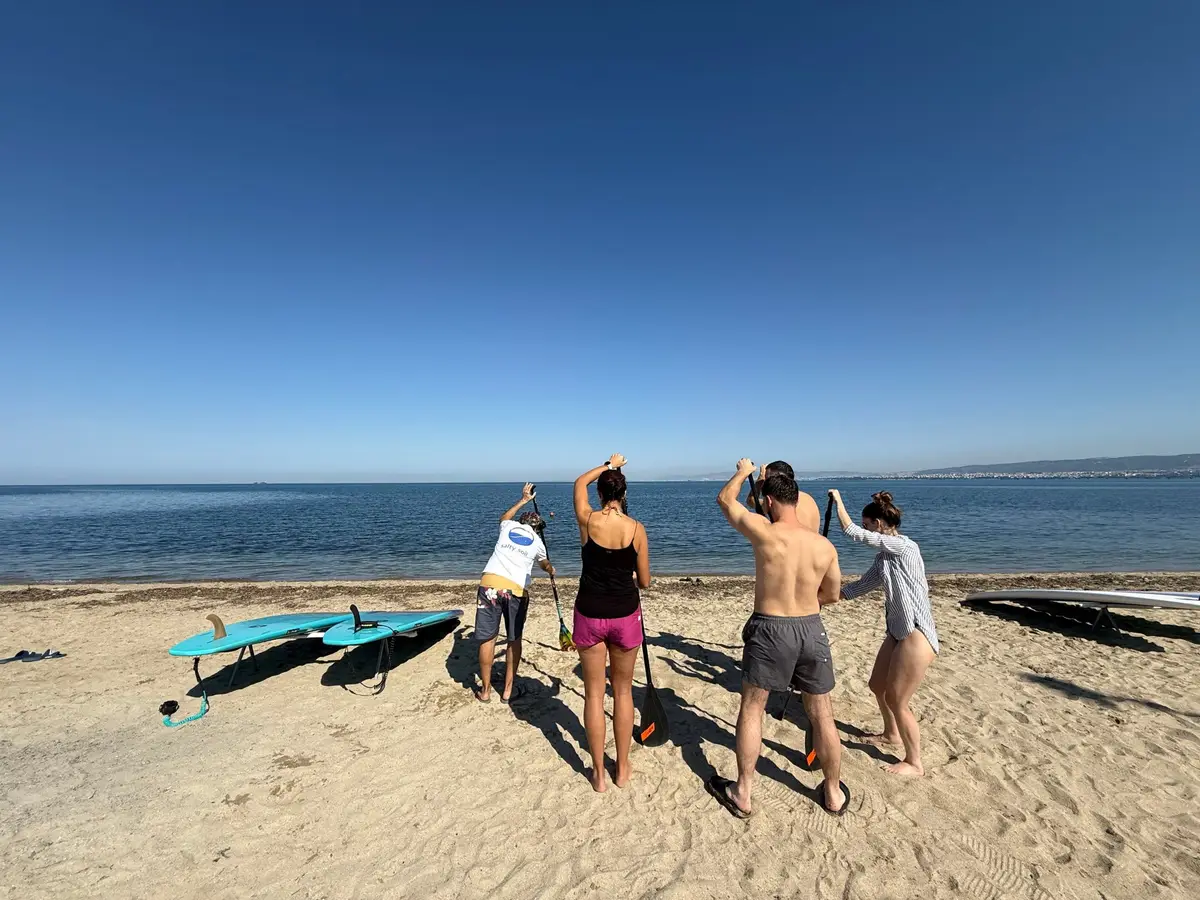 A Salty Soil instructor leads a paddle warm-up on the beach at Perea, with Thessaloniki across the bay