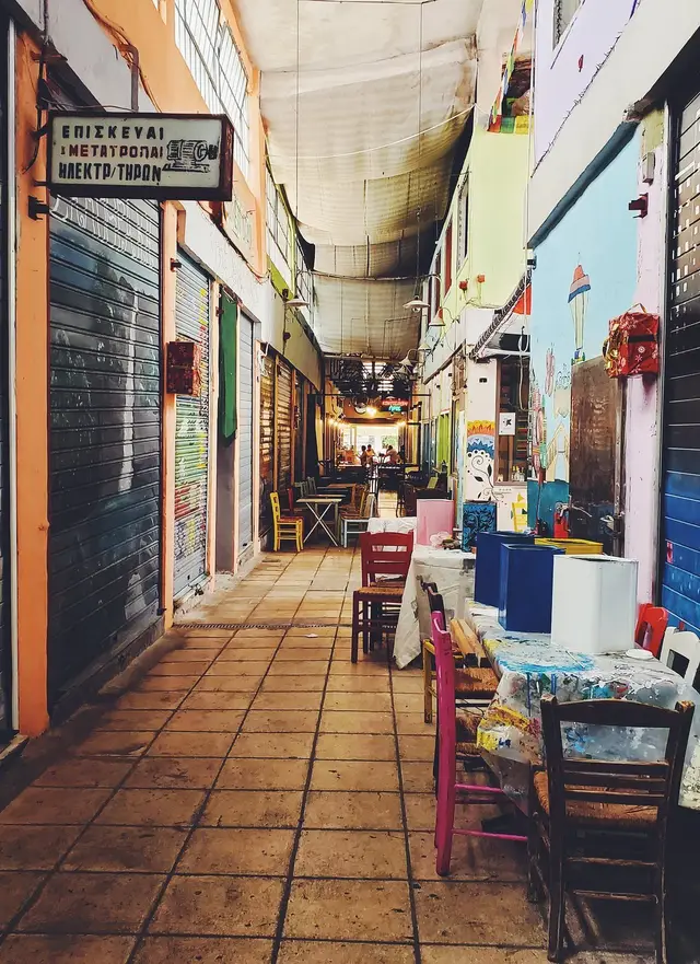 A covered passage of old small shops with painted shutters and taverna tables in central Thessaloniki, on the Salty Soil food tour route