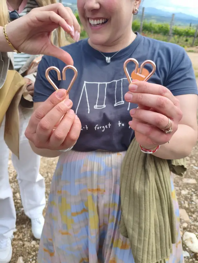 A player holds up two pieces of a heart-shaped metal puzzle at a vineyard during a Salty Soil treasure hunt at a winery