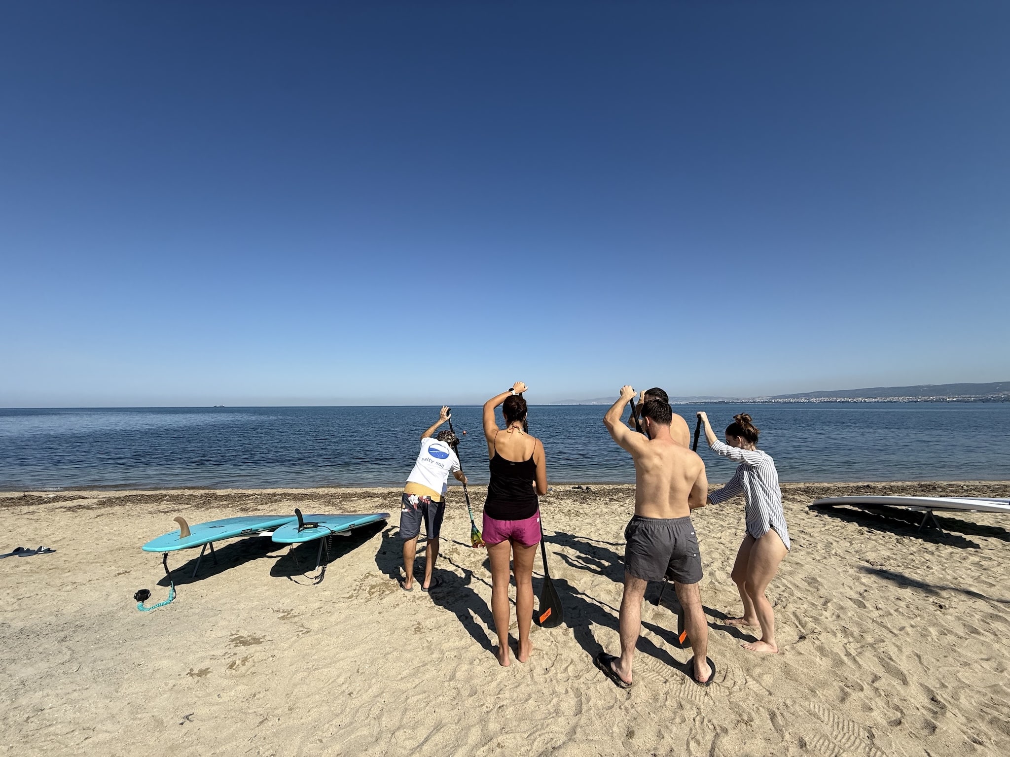 Salty Soil guide demonstrating paddle technique to a small group on the beach before a stand-up paddleboard tour near Thessaloniki, boards resting on the sand